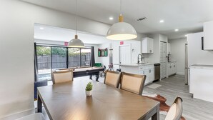 A modern kitchen with white cabinets, a dining area with a wooden table and chairs, and a view of a backyard.