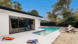 A modern house with a swimming pool, a patio with lounge chairs, and a large sliding glass door.