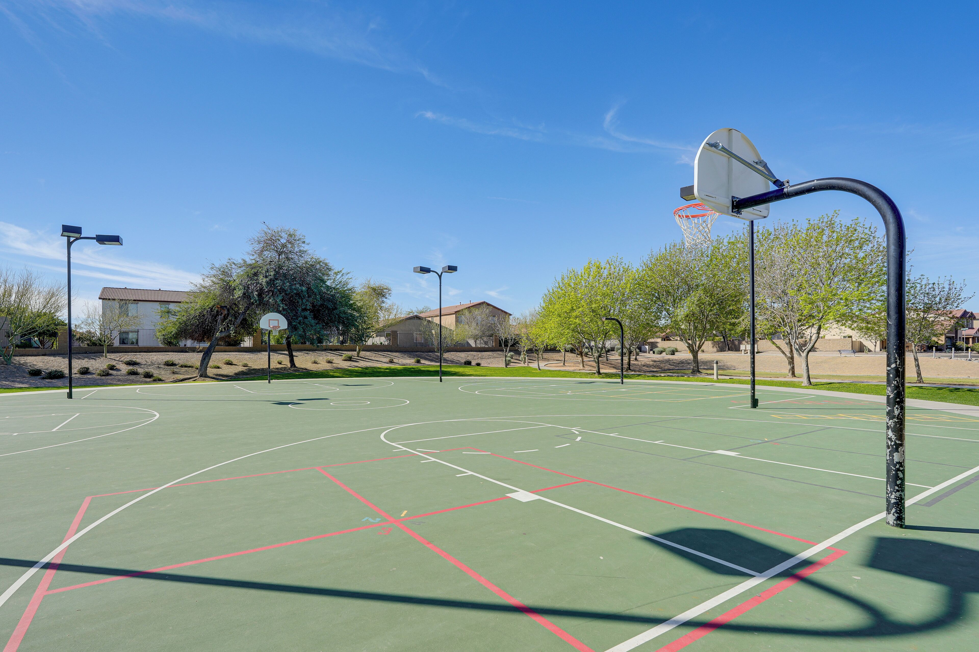 An outdoor basketball court with clear markings, street lamps, and trees.