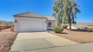 A single-story house with a white garage door, a small front yard with a gravel driveway, and a tall tree to the right.