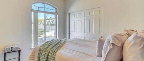 A bedroom with a large bed, a window, a door, and a small table with towels.