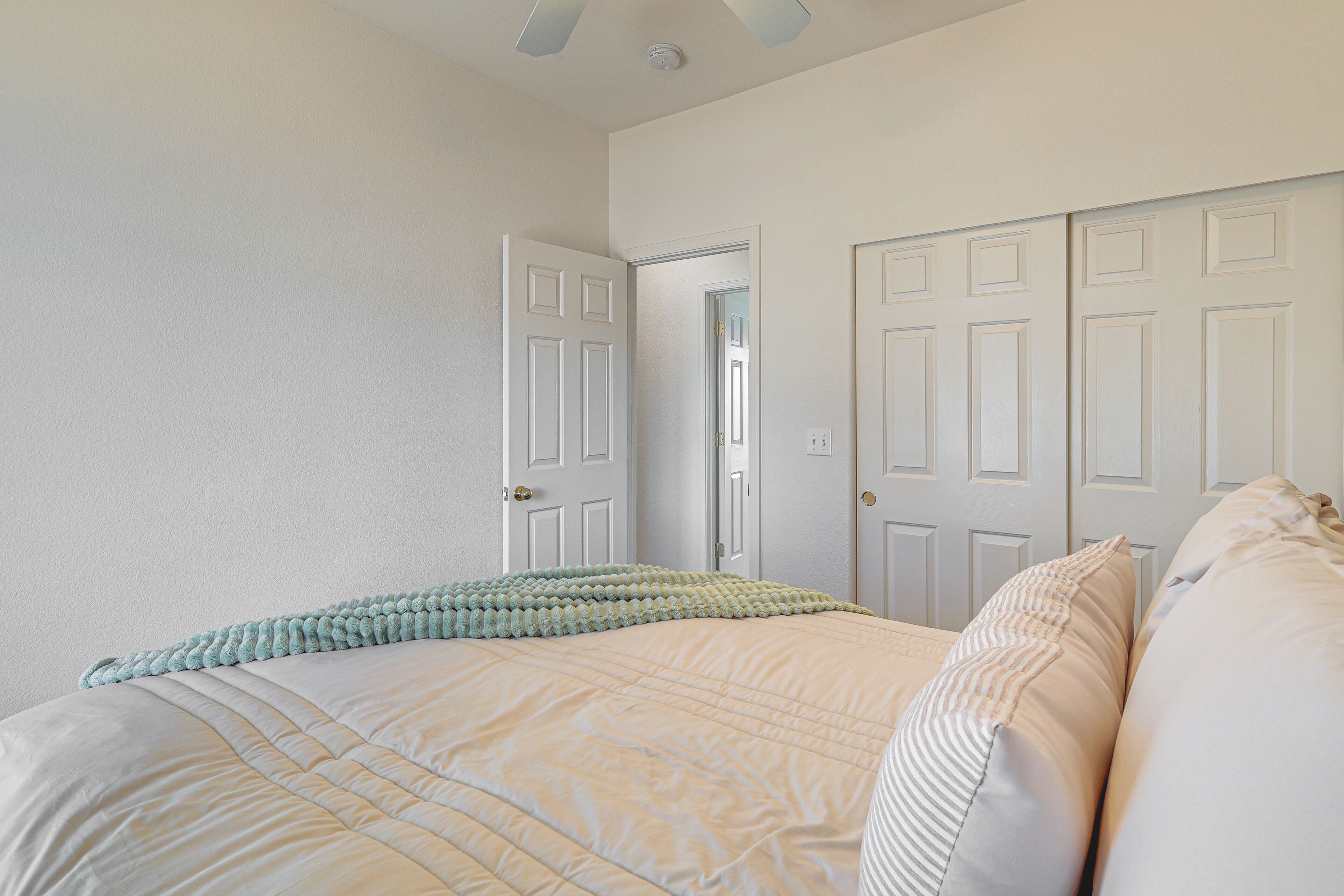 A bedroom with a large bed, white walls, and a door leading to another room.