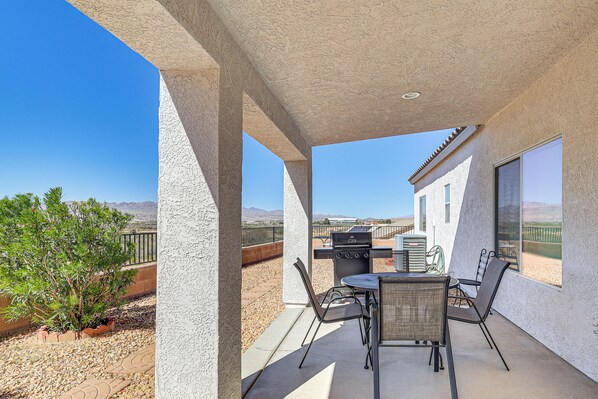 Eine überdachte Terrasse mit Grill, Sitzgelegenheit und Blick auf die Wüstenlandschaft.