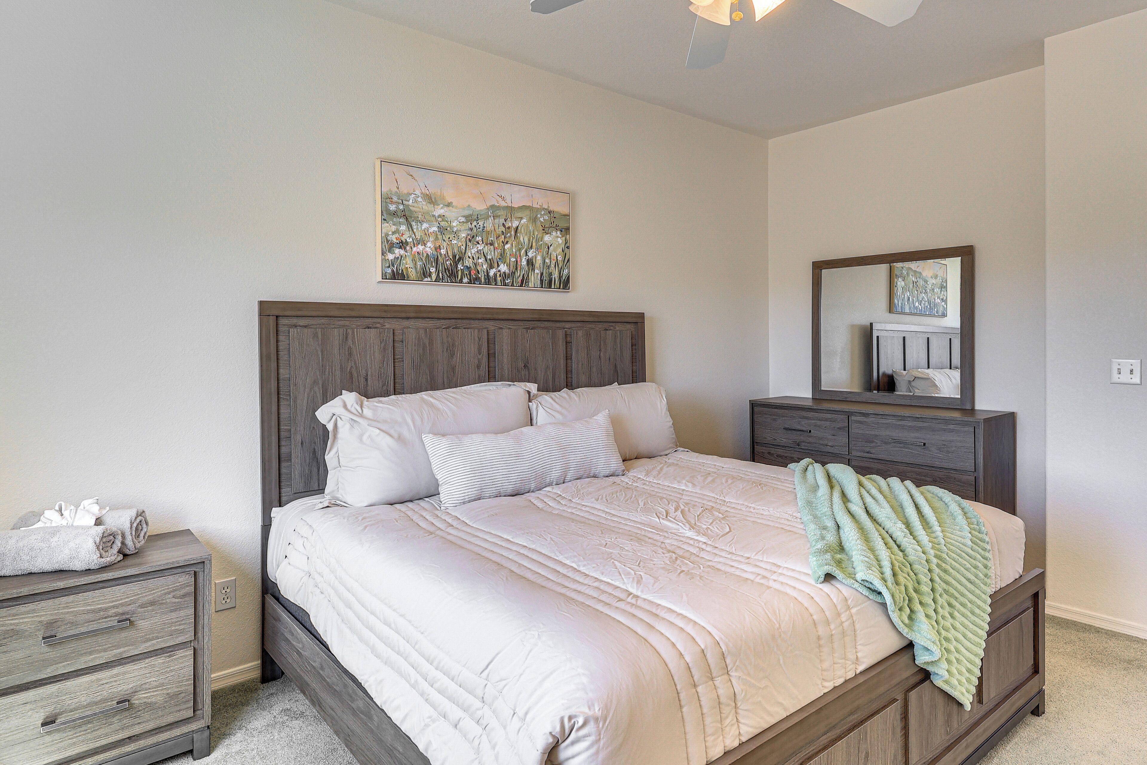 A bedroom with a wooden bed frame, a bedside table, a dresser, and a ceiling fan.