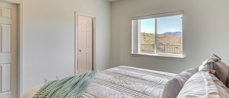 A bedroom with a bed, a window with a view of a desert landscape, a ceiling fan, and a door.