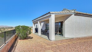 A covered patio with a barbecue, outdoor seating, and a view of the desert landscape.