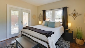 A bedroom with a bed, bedside tables, a ceiling fan, a window with curtains, a door leading to a patio, and a wall-mounted decorative item. - Walk to Fishing Pond! Wooded Montgomery Retreat (Montgomery)
