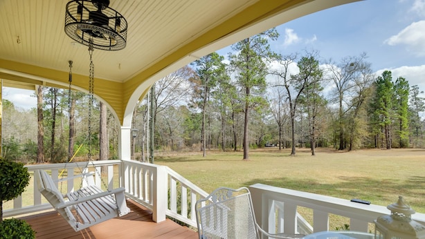 A porch with a white railing, a hanging chair, and a table with a lantern. - Walk to Fishing Pond! Wooded Montgomery Retreat (Montgomery)