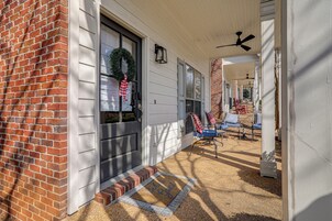A covered porch with a brick wall, a door with a wreath, and a bench with a red and white checkered blanket.