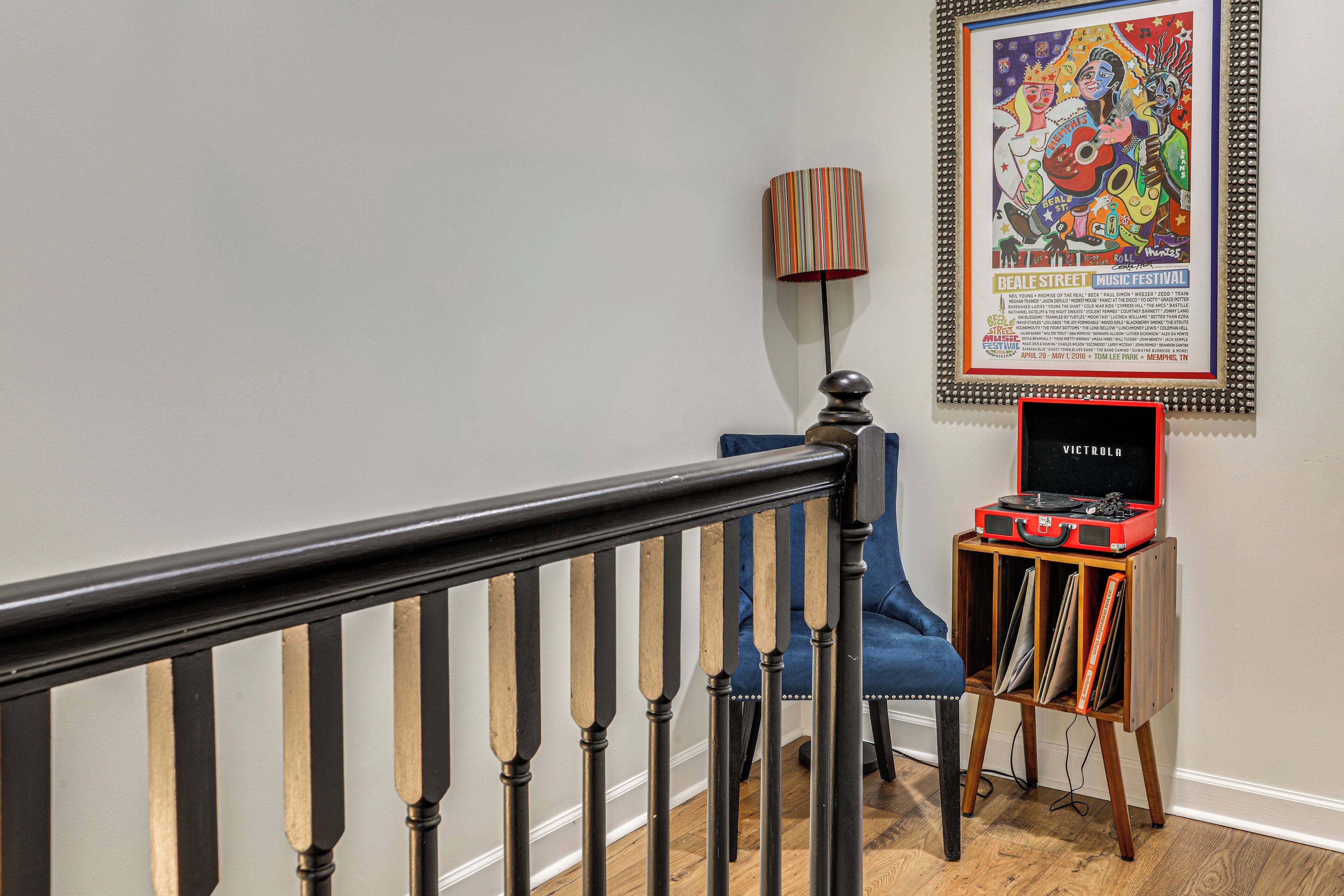 Eine Treppe mit schwarzer Handlauf, einem blauen Stuhl, einer Lampe und einem gerahmten Plakat an der Wand.