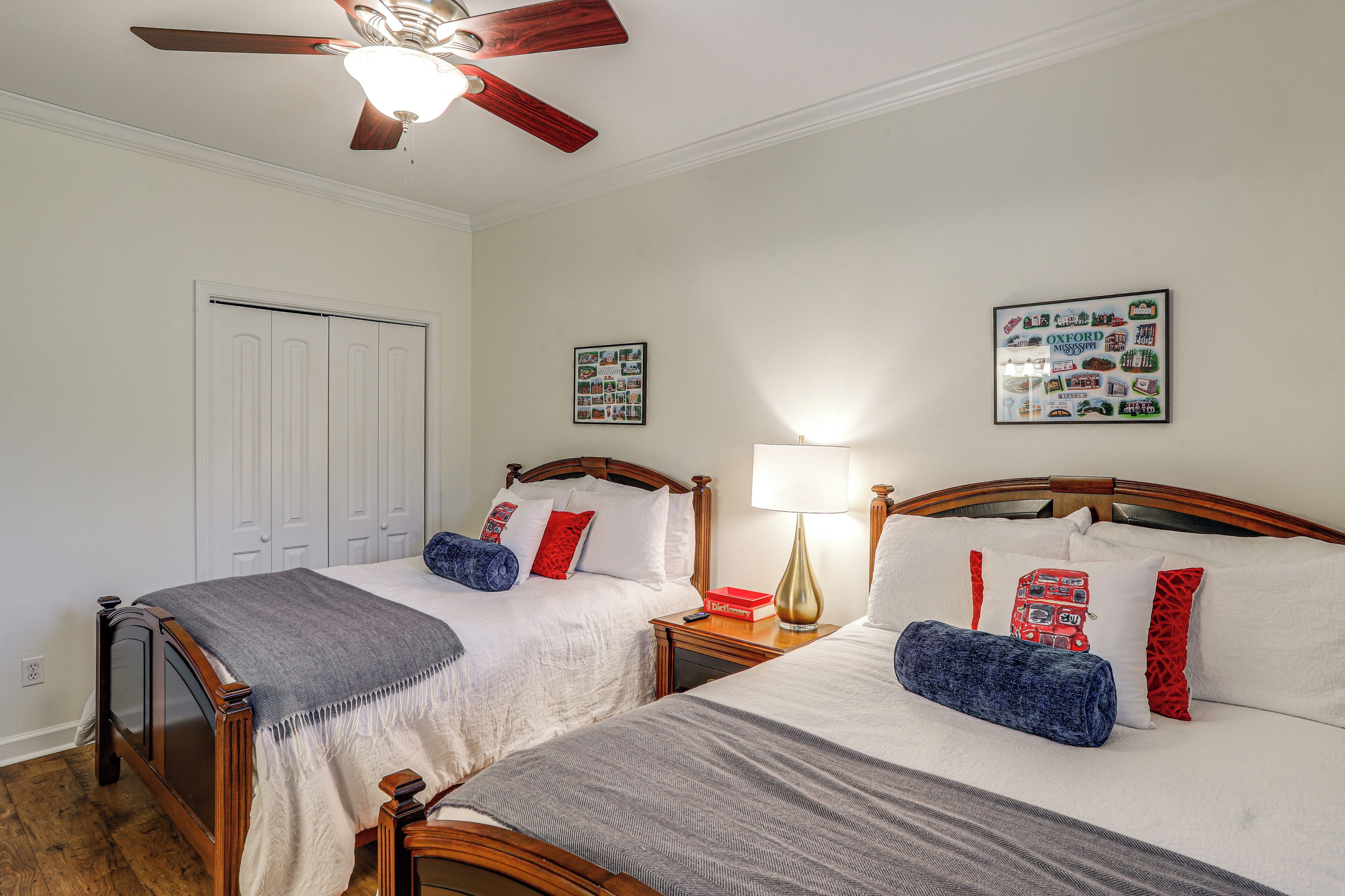 A bedroom with two beds, a ceiling fan, a nightstand, and a wall with a framed picture.
