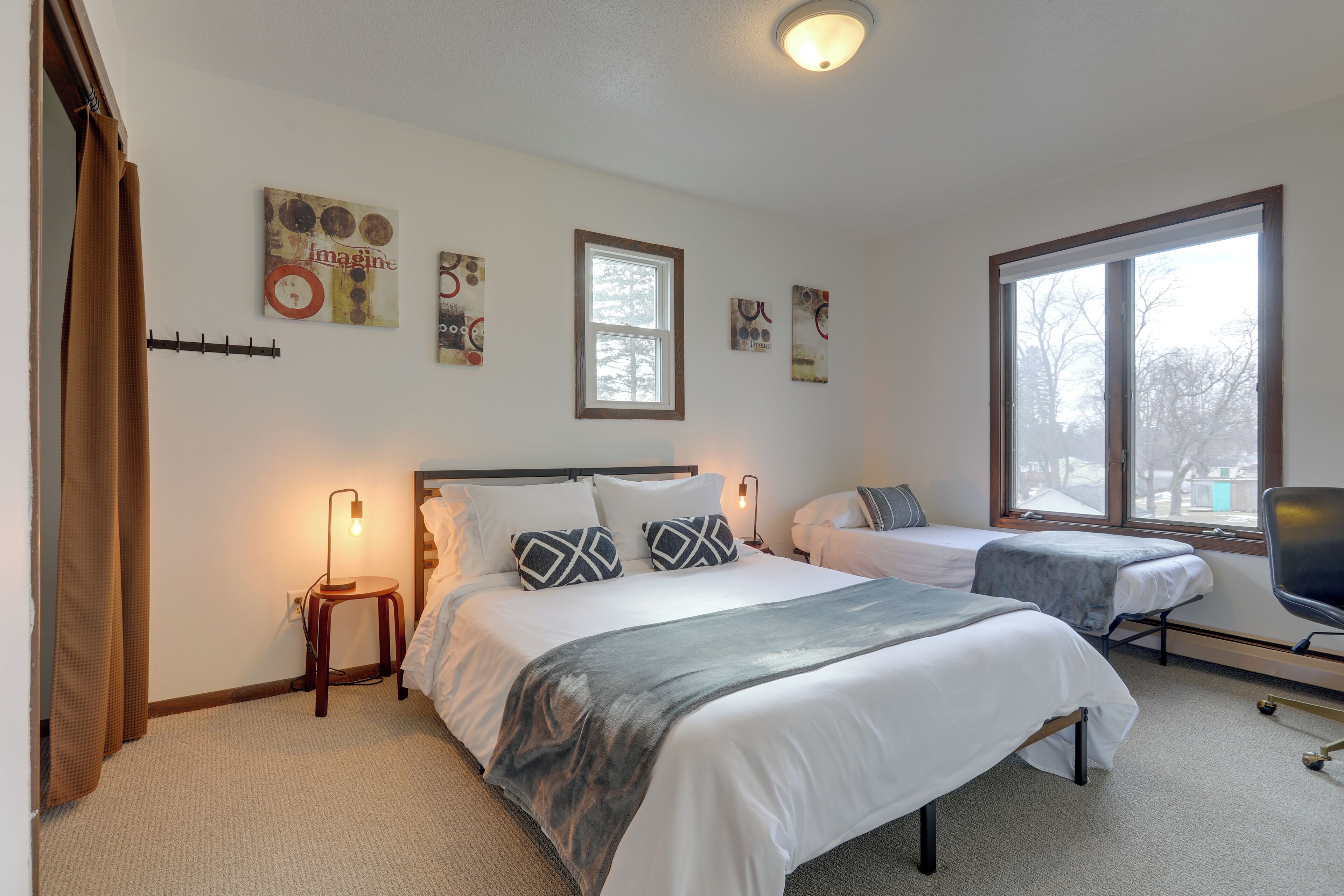 A hotel room with two beds, a desk, a chair, and artwork on the walls.
