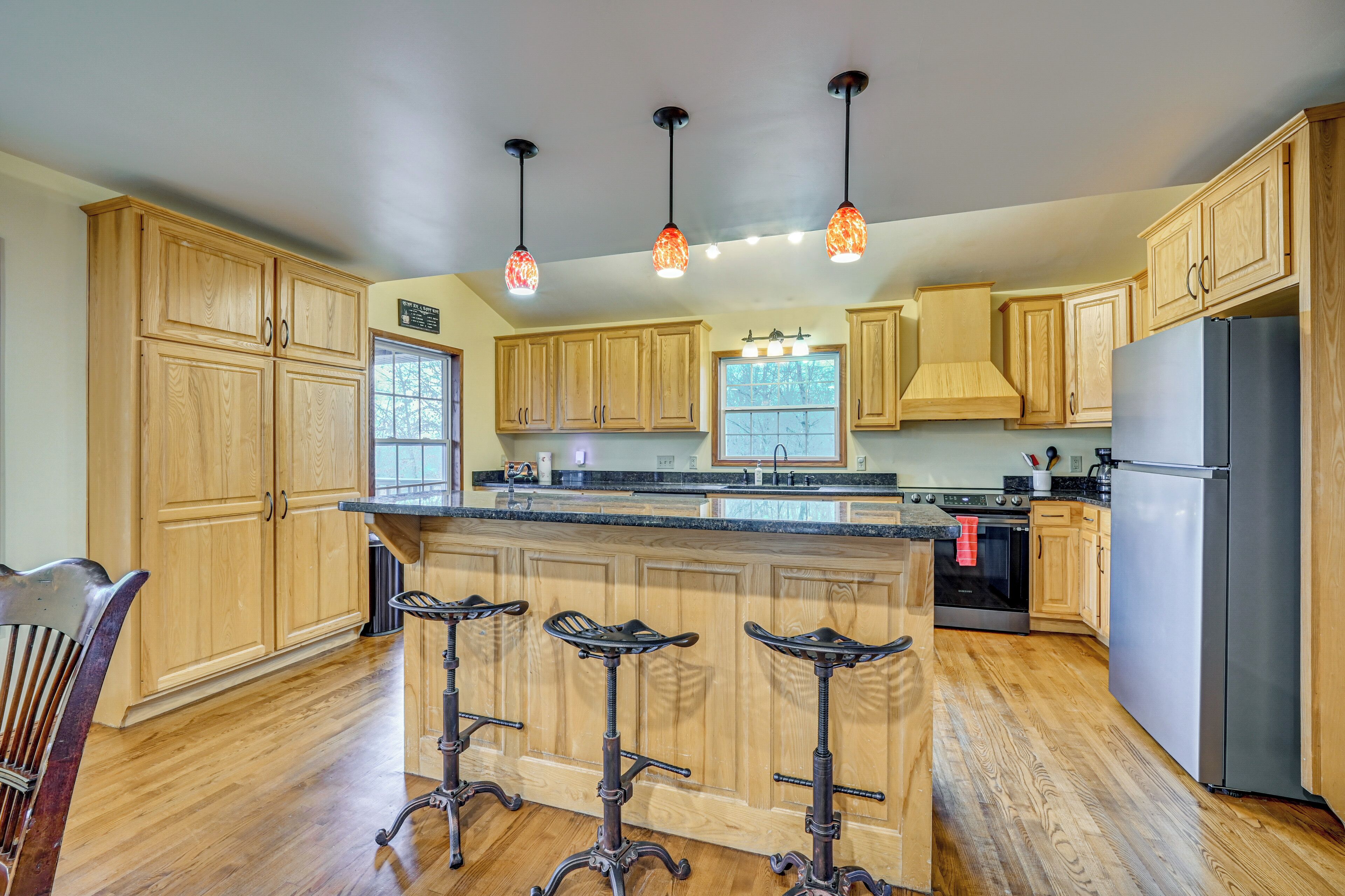 A kitchen with wooden cabinets, a stainless steel refrigerator, and three bar stools.