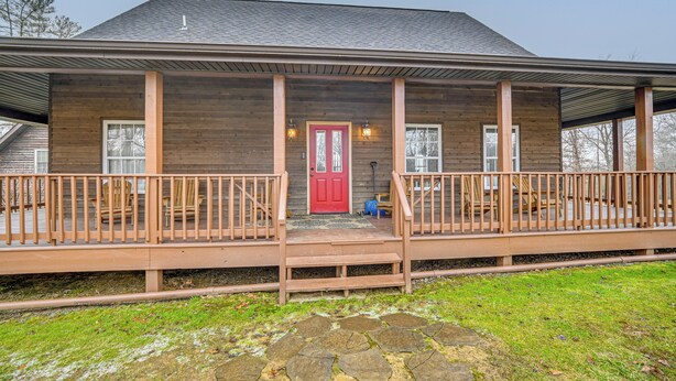 A wooden house with a red door, two balconies, and a stone pathway leading to the entrance.