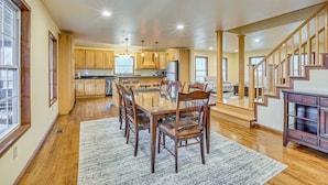 A spacious kitchen with wooden cabinets, a dining area with a glass table, and a staircase leading to another level.