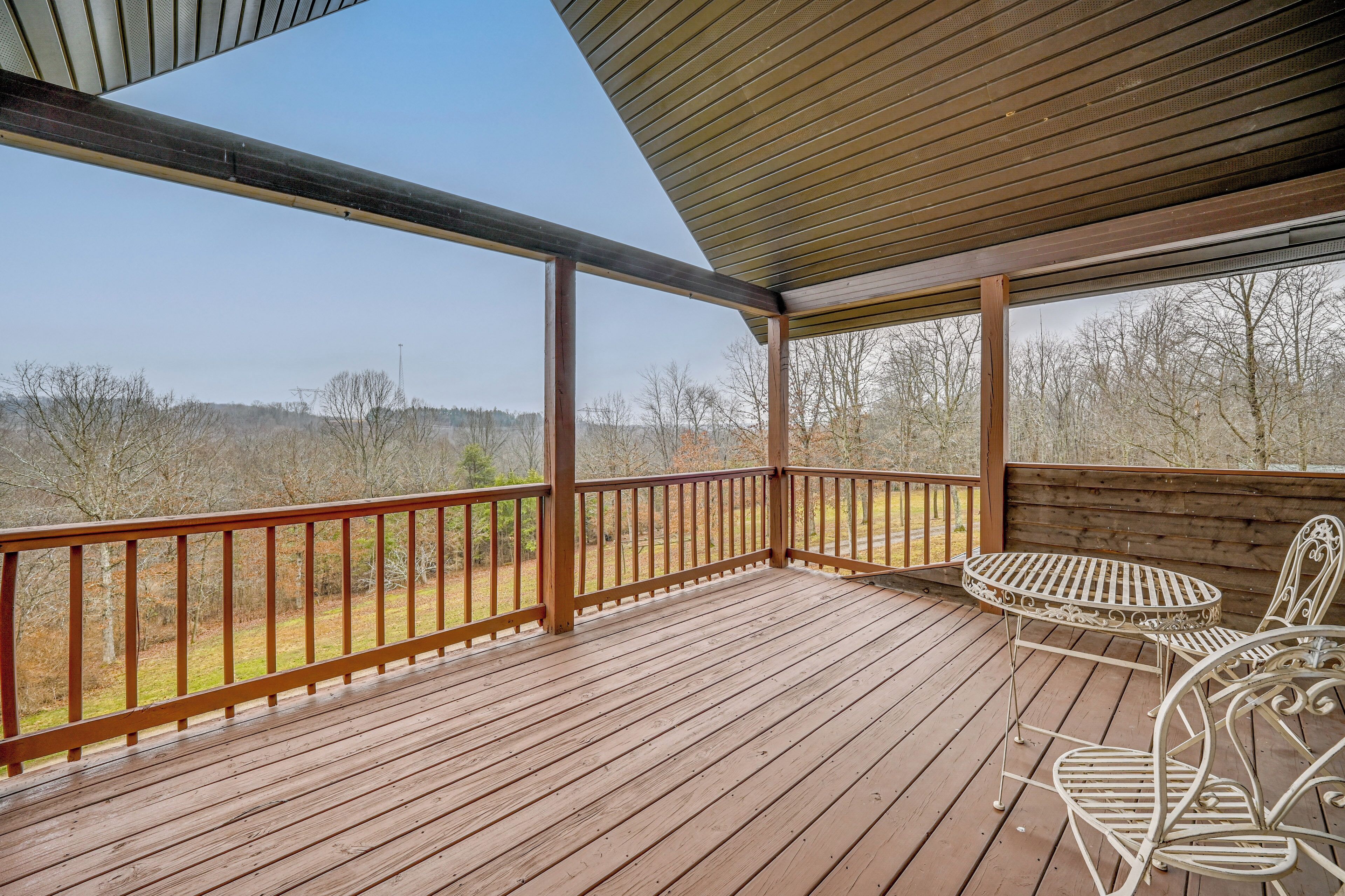 A wooden deck with a metal table and chairs, overlooking a forested area.