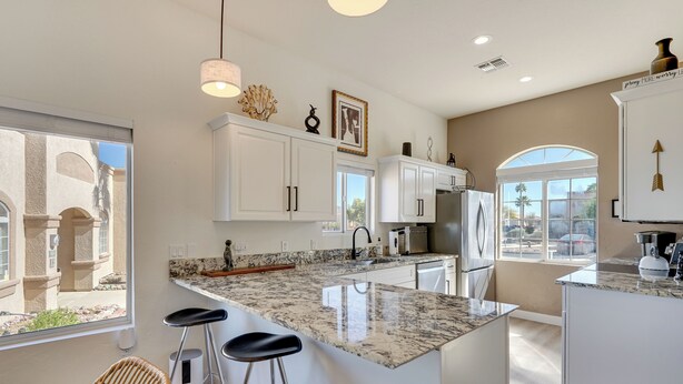 A modern kitchen with white cabinets, a granite countertop, and a large island with bar stools. - Private Golf Cart! 55-plus Green Valley Getaway (Green Valley)