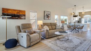 A modern living room with a sofa, armchair, and coffee table, a dining area with chairs, and a kitchen in the background. - Private Golf Cart! 55-plus Green Valley Getaway (Green Valley)