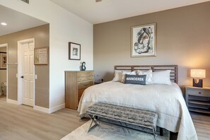 Ein Schlafzimmer mit Bett, Sitzbank, Nachttisch, Lampe und Kunstwerk an der Wand.
