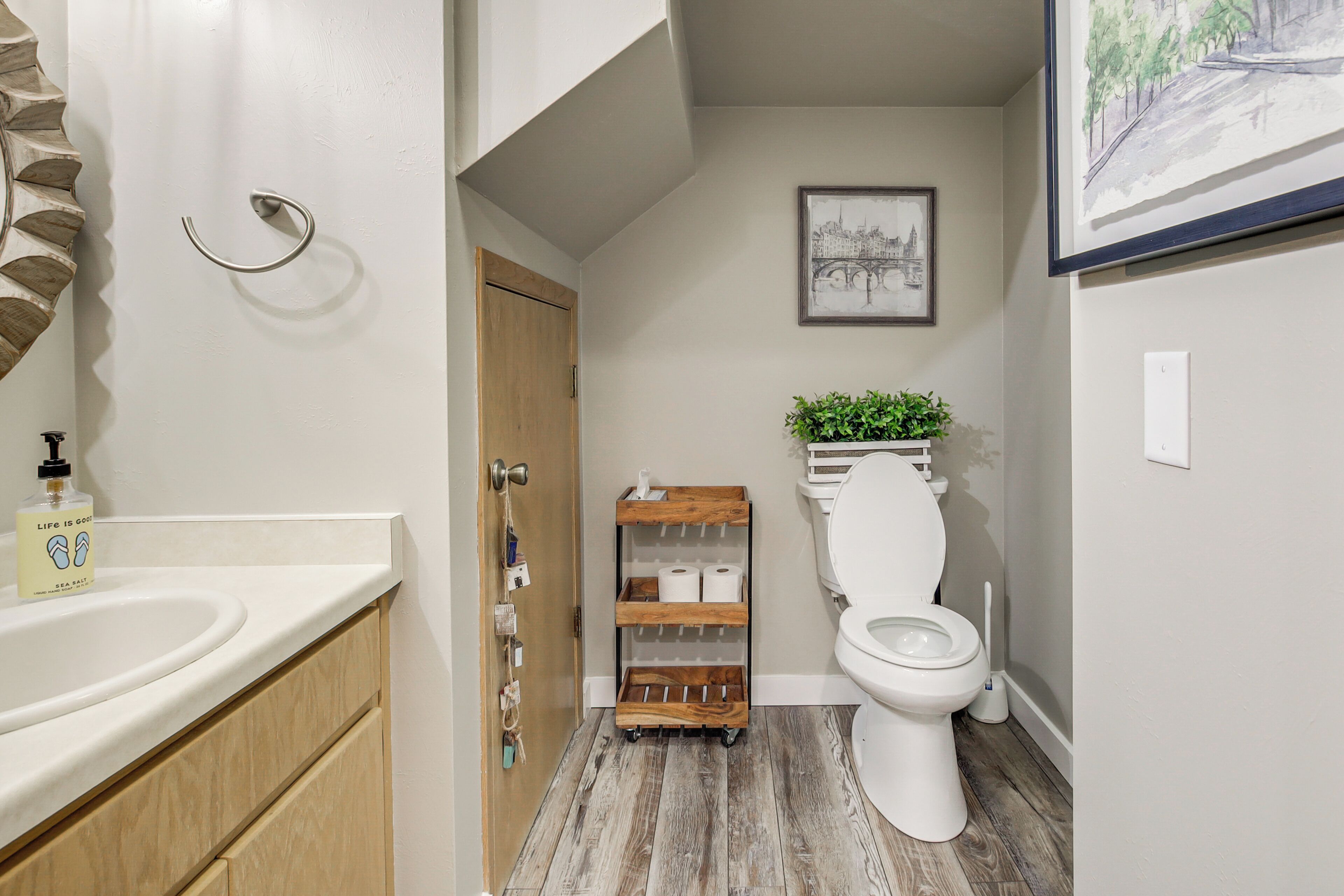 Un baño con suelo de madera, inodoro blanco y un estante con artículos de aseo.