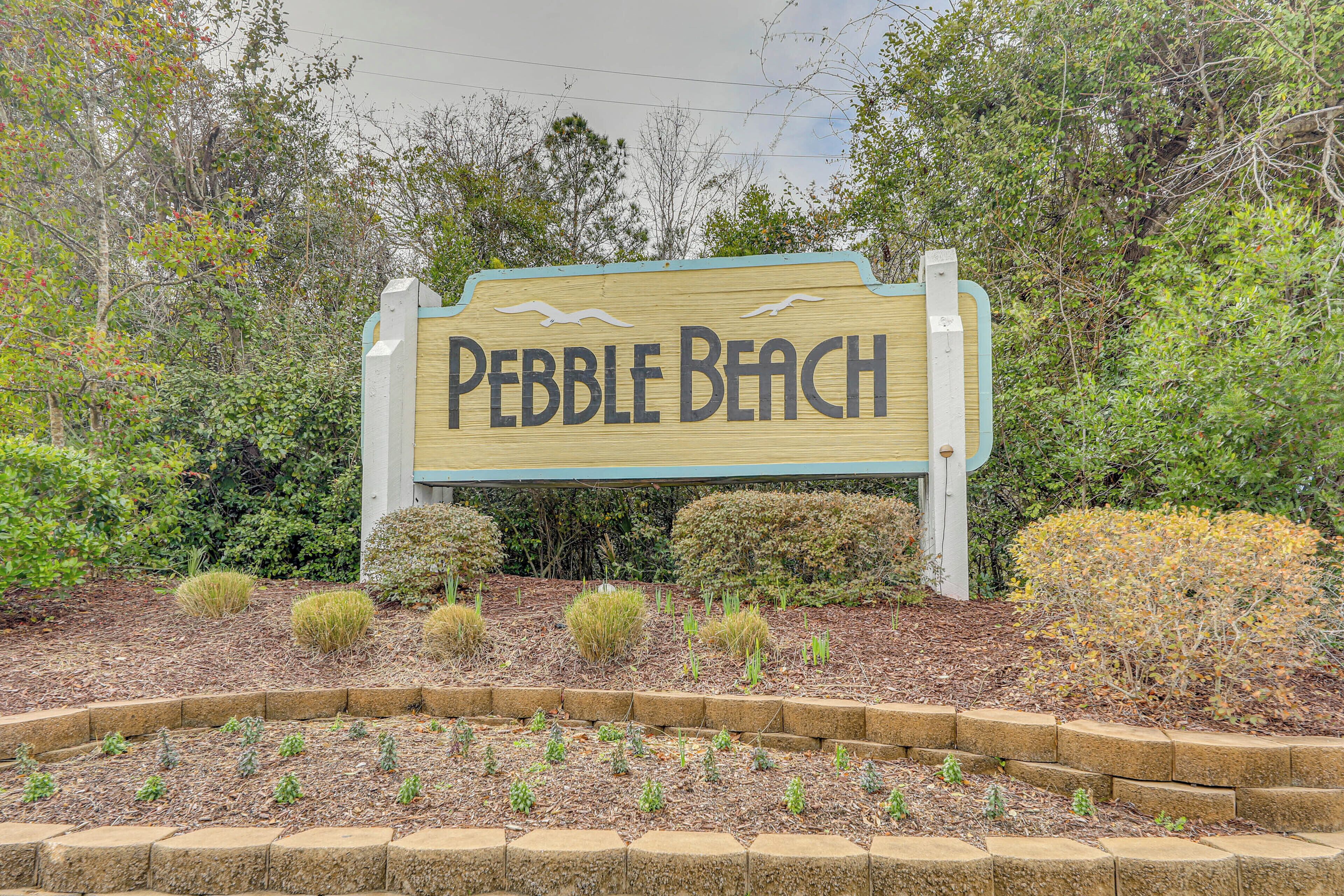 Un panneau en bois portant l’inscription « Pebble Beach », entouré de parterres aménagés et de divers arbustes.