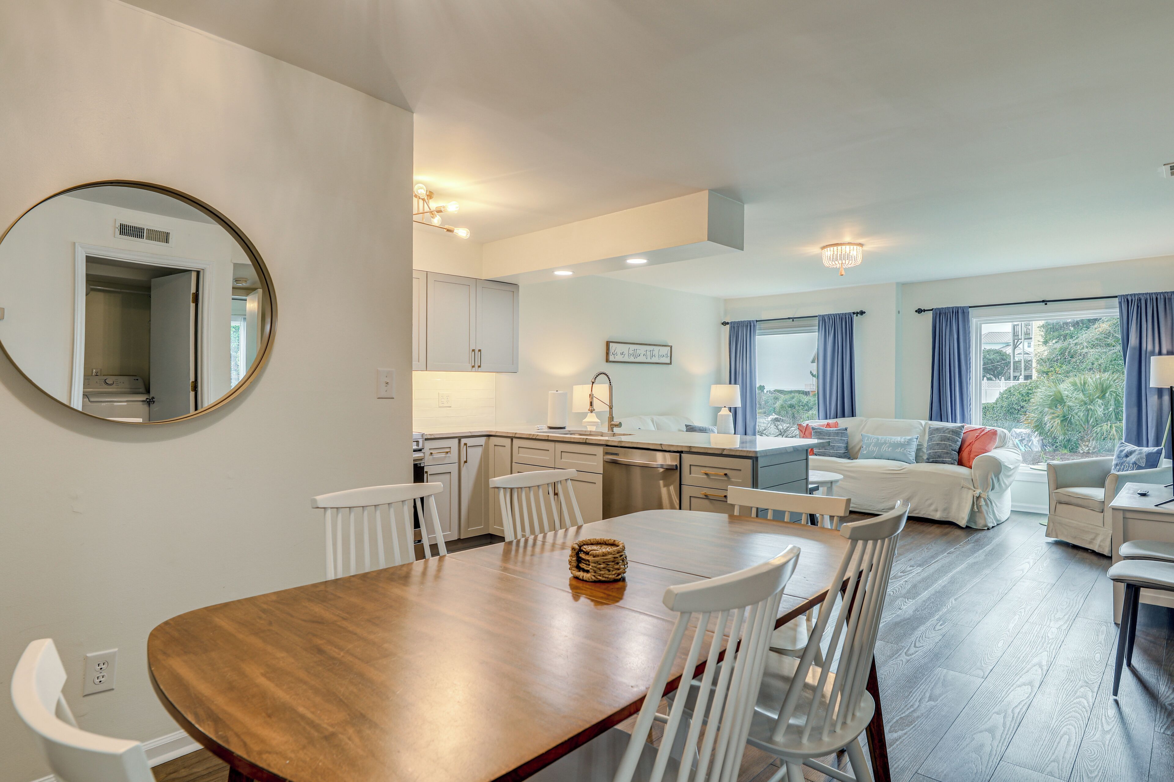 A modern kitchen with white cabinets, a dining area with a wooden table and white chairs, and a living area with a sofa and armchairs.
