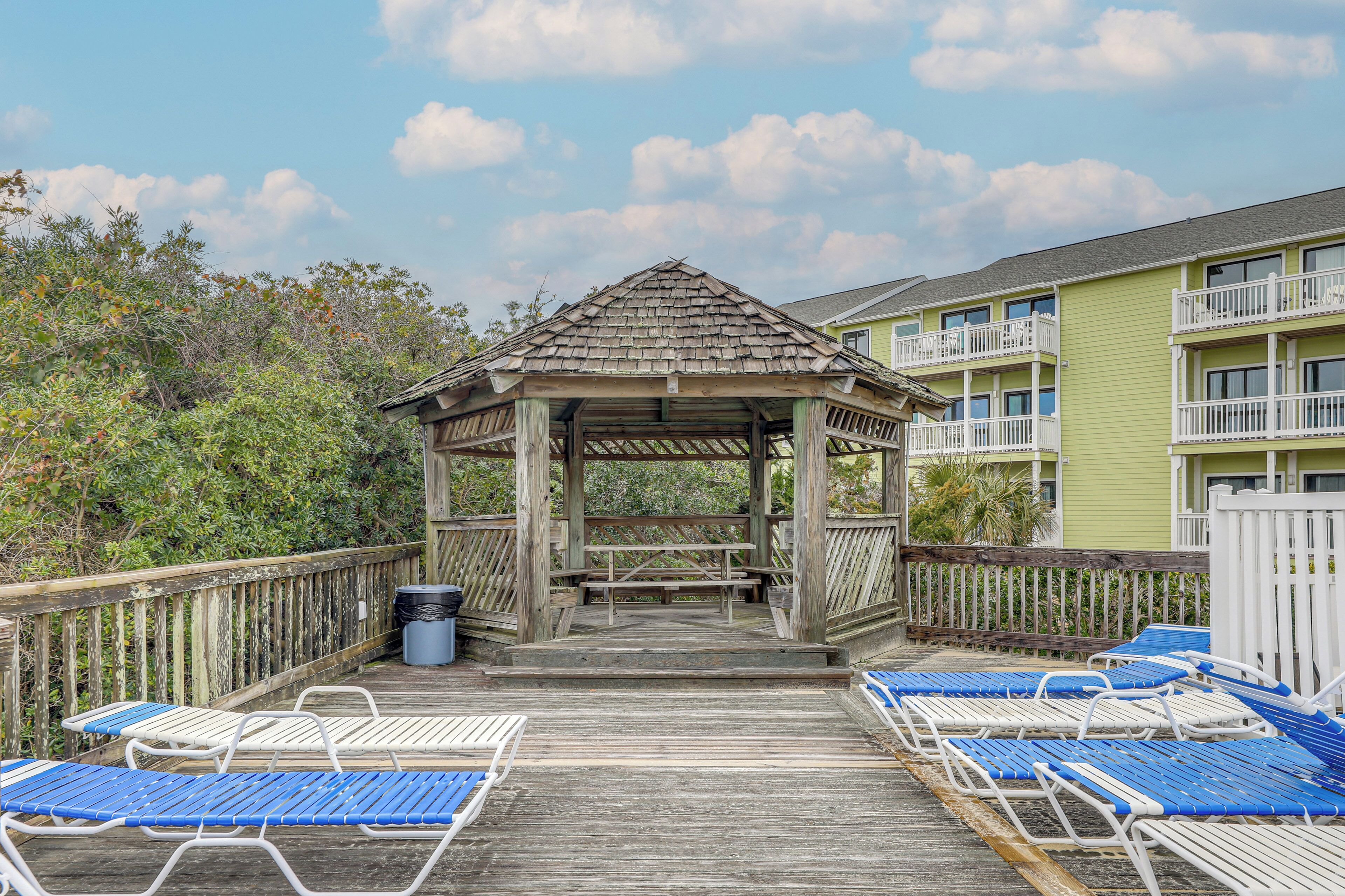 A wooden deck with blue and white lounge chairs, a gazebo, and a building with balconies in the background.