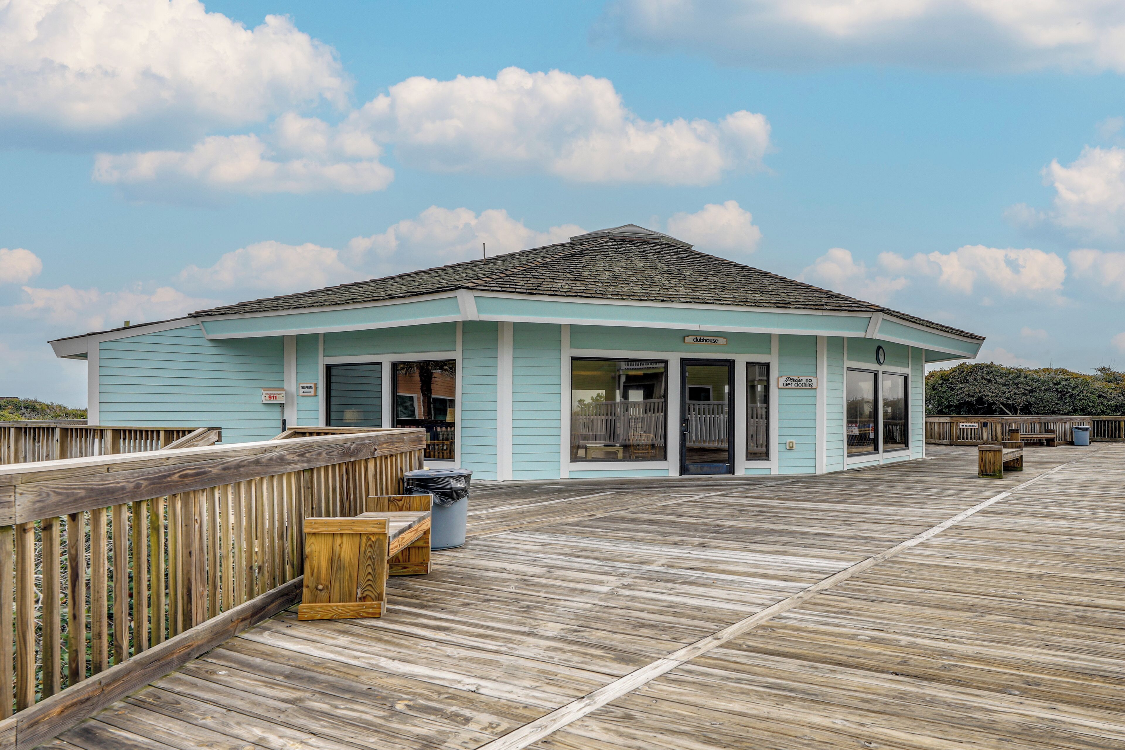 A light blue building with a wooden deck, a wooden fence, and a trash bin.