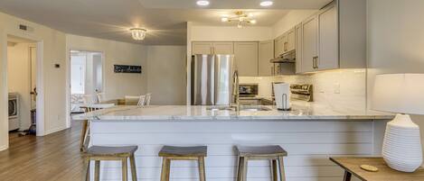 A modern kitchen with a central island, wooden stools, and stainless steel appliances.