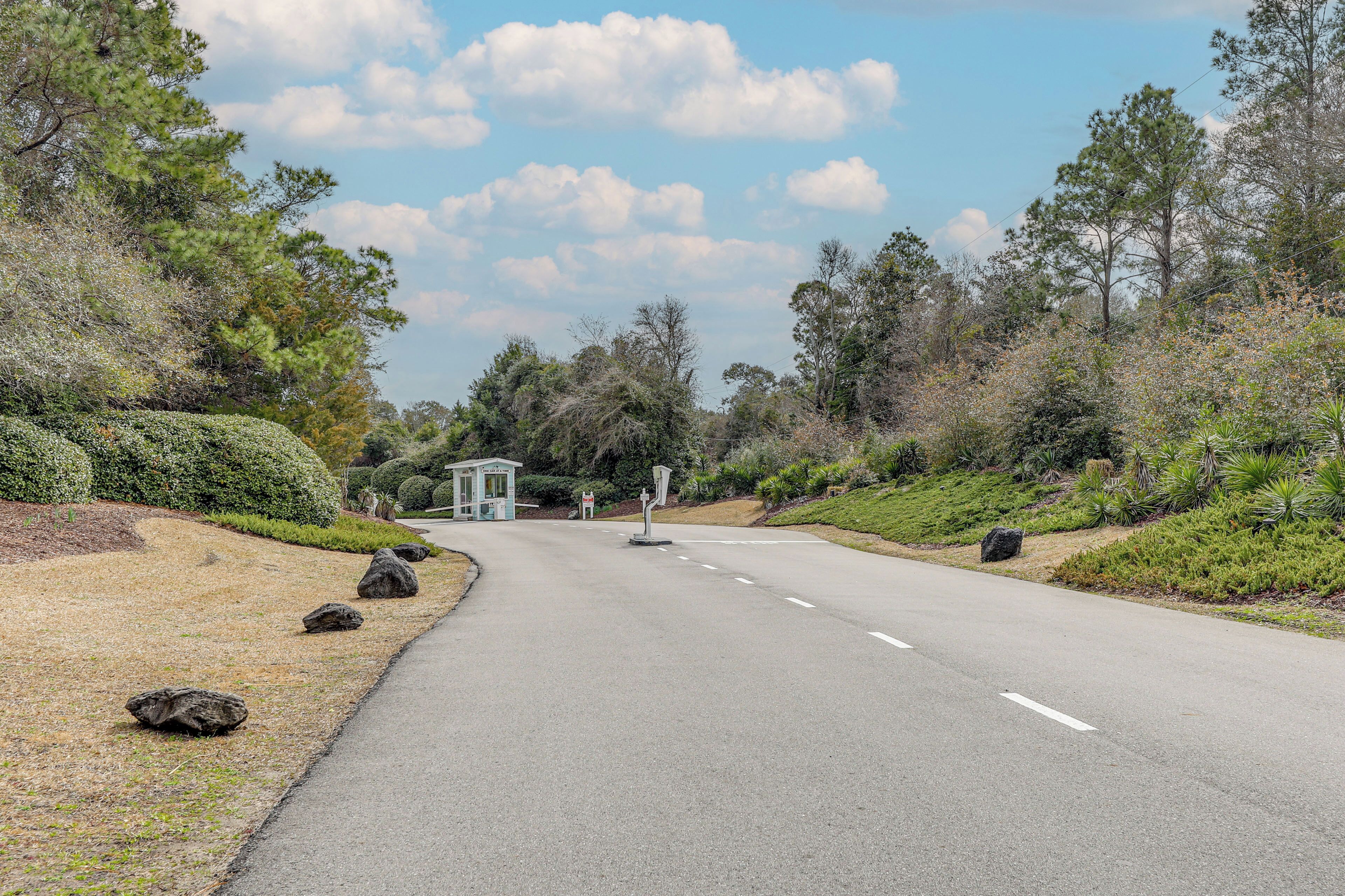 A road with a gazebo-like structure in the distance, surrounded by trees and shrubs.