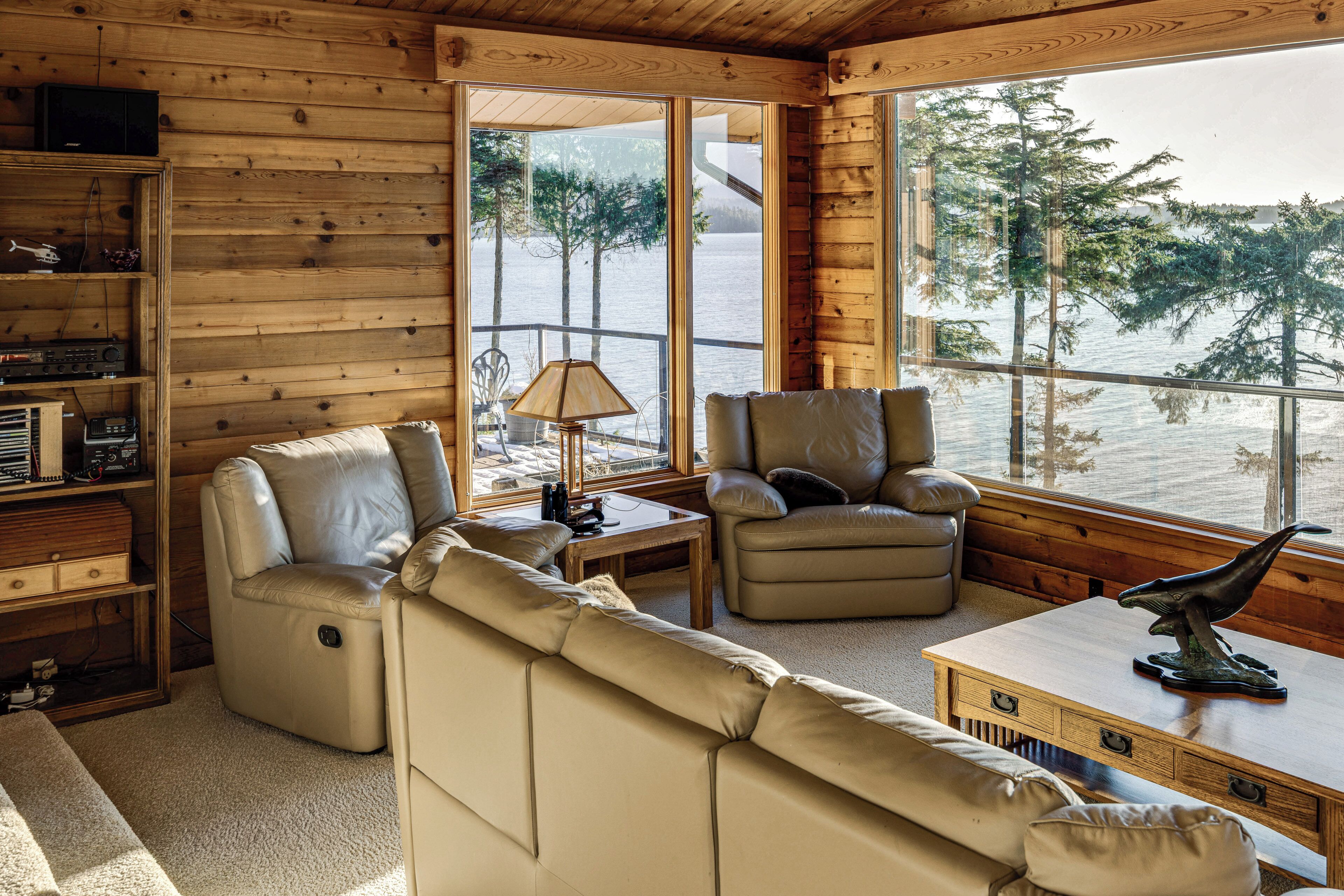Interior acogedor de una cabaña con sofá, sillón y una mesita de centro. Se aprecia también una estantería y una lámpara.