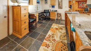 Une pièce spacieuse et bien éclairée, avec un grand bureau, un fauteuil confortable, un globe terrestre posé sur une commode et un tapis à motifs.