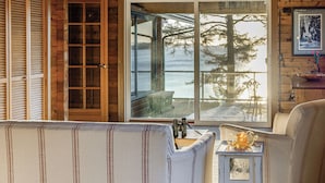 Une pièce chaleureuse avec une grande fenêtre donnant sur un lac et des arbres. Un banc rembourré se trouve près de la fenêtre, ainsi qu'une petite table sur laquelle est posé un objet décoratif.
