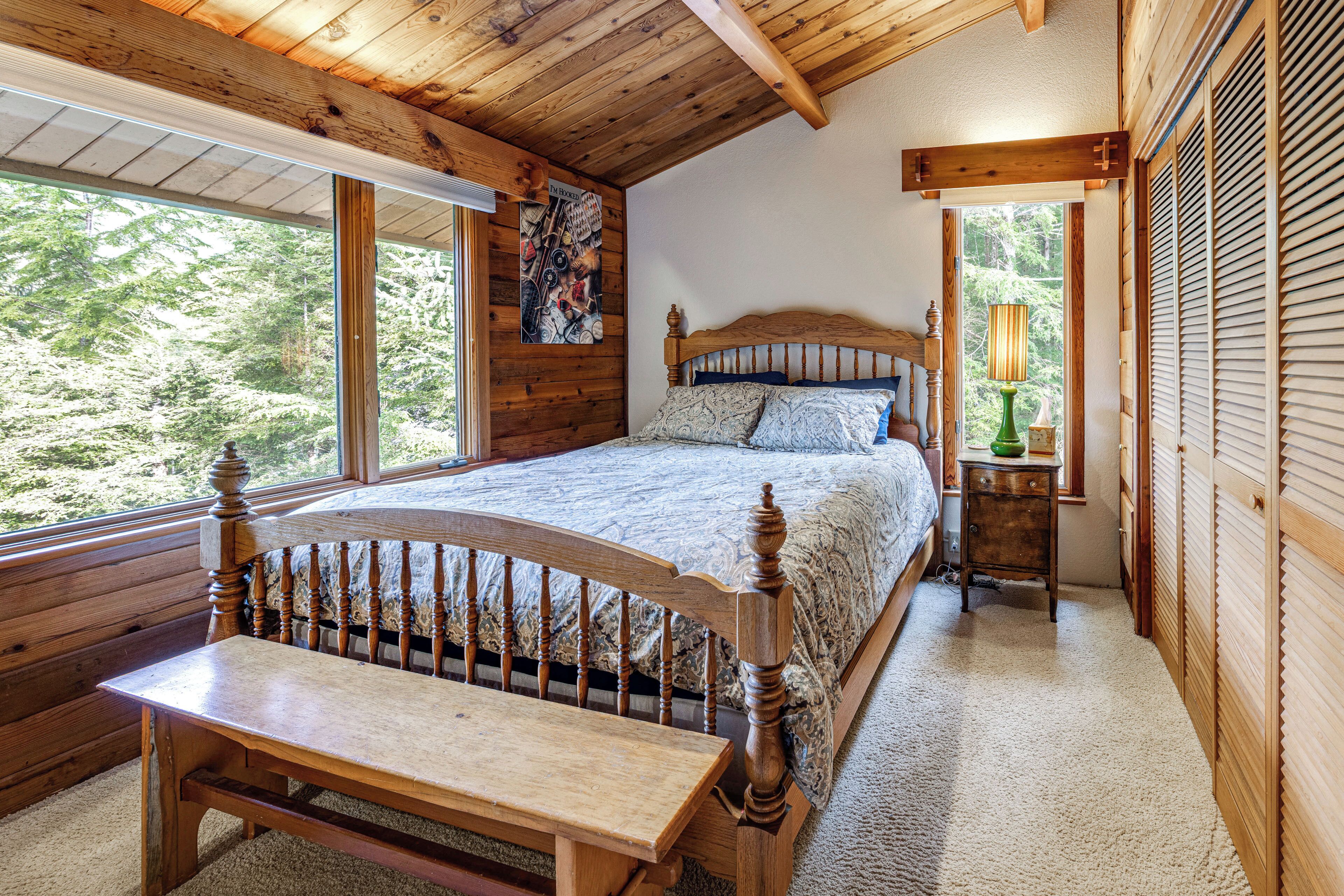 A wooden bedroom with a large bed, a wooden bench, and a window with a view of trees.