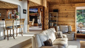 L’intérieur d’un chalet confortable, avec un canapé, des fauteuils, une cheminée et une bibliothèque.