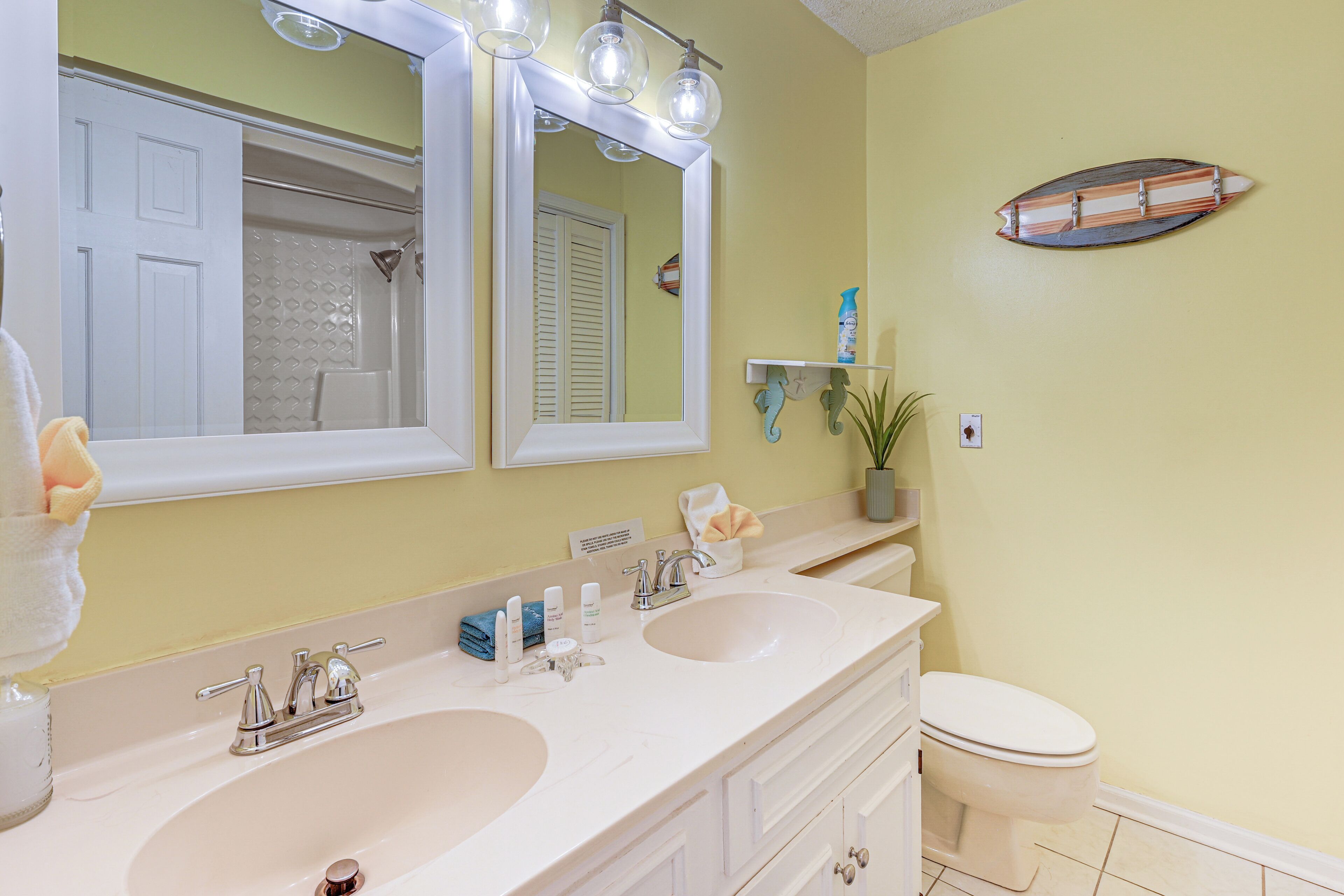 A bathroom with two sinks, a toilet, a mirror, and a shelf with toiletries.