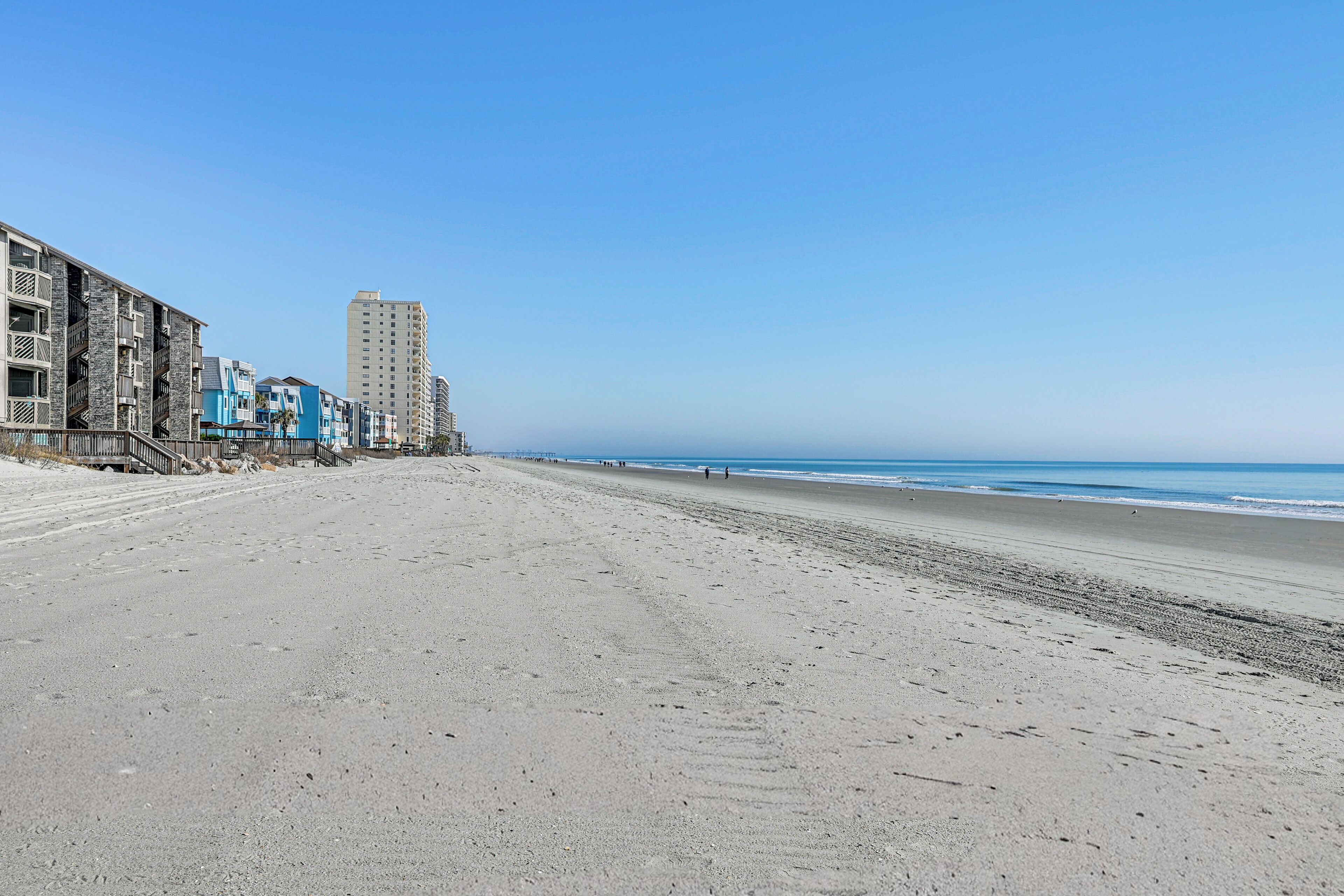 A beach with a row of buildings, including a tall hotel, and a clear blue sky.