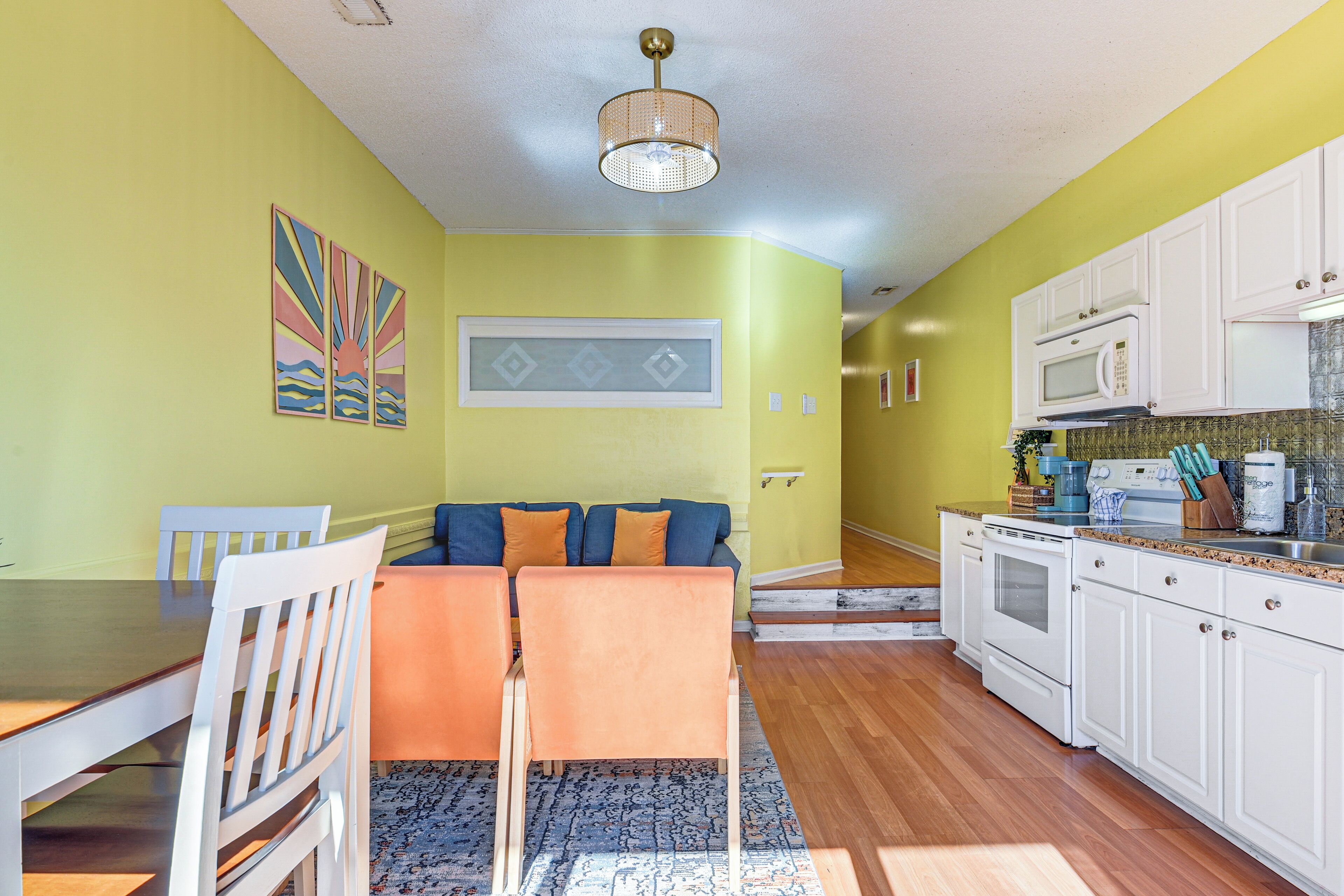 A kitchen with white cabinets, a microwave, and a stove. There is a dining area with a table and chairs.