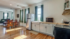 Una cocina amplia con piso de madera, armarios blancos, un refrigerador de acero inoxidable y un comedor con sillas y una mesa de madera.