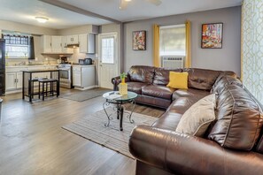 A modern kitchen with white cabinets, a dining area with a brown leather couch, and a small round table with a vase.