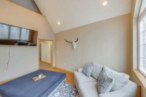 A room with a sofa, a table with a tray, a wall-mounted TV, and a bull skull decoration.
