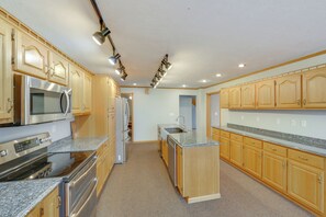 A kitchen with wooden cabinets, stainless steel appliances, granite countertops, and under-cabinet lighting.