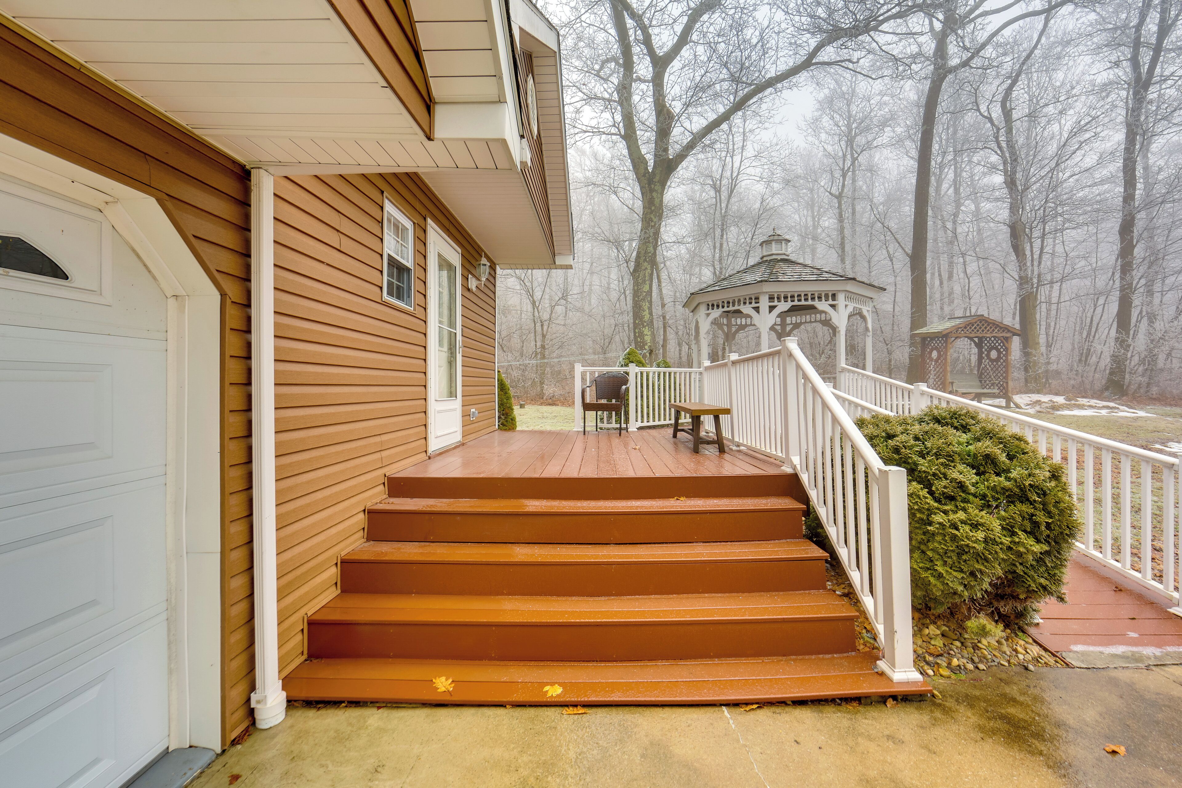 A wooden house with a porch, steps, and a gazebo in the background.