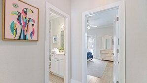 Un pasillo que conduce a un baño con puerta blanca, un cuadro abstracto enmarcado en la pared y una zona de ducha visible.