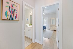 Ein Flur, der zu einem Badezimmer mit weißer Tür führt, mit einem Bilderrahmen mit einem abstrakten Gemälde an der Wand und einem sichtbaren Duschbereich.
