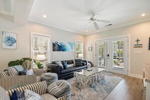 A spacious living room with a black leather sofa, striped armchairs, a glass coffee table, and a ceiling fan. - Freestanding 3br with tiki bar and pool (Pensacola)