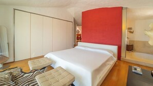 Ett hotellrum med en säng, en röd accentvägg, en stor spegel, ett trägolv och en sittgrupp med en matta i zebrastripmönster.