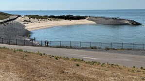 A coastal landscape with a sandy beach, a rocky breakwater, and a paved walkway. - White Beach House (Breskens)