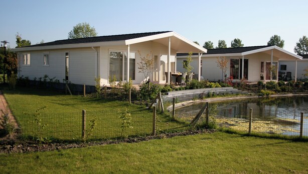 A modern two-story house with a covered porch, a small pond, and a fenced yard. - White Beach House (Breskens)