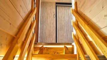 Una escalera de madera que lleva a un altillo con pared de ladrillo y una ventana.
